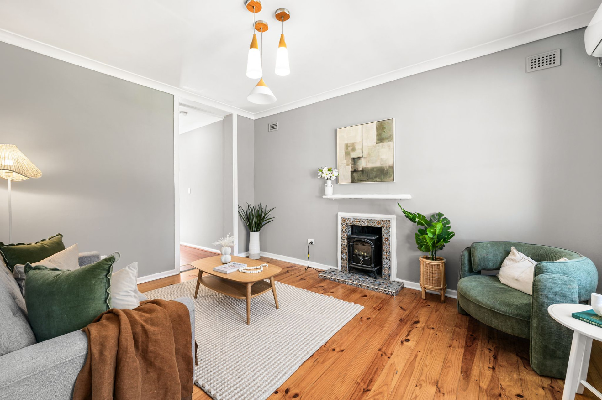 Separate living room with timber flooring, sofas, coffee table, fireplace, plants and artwork