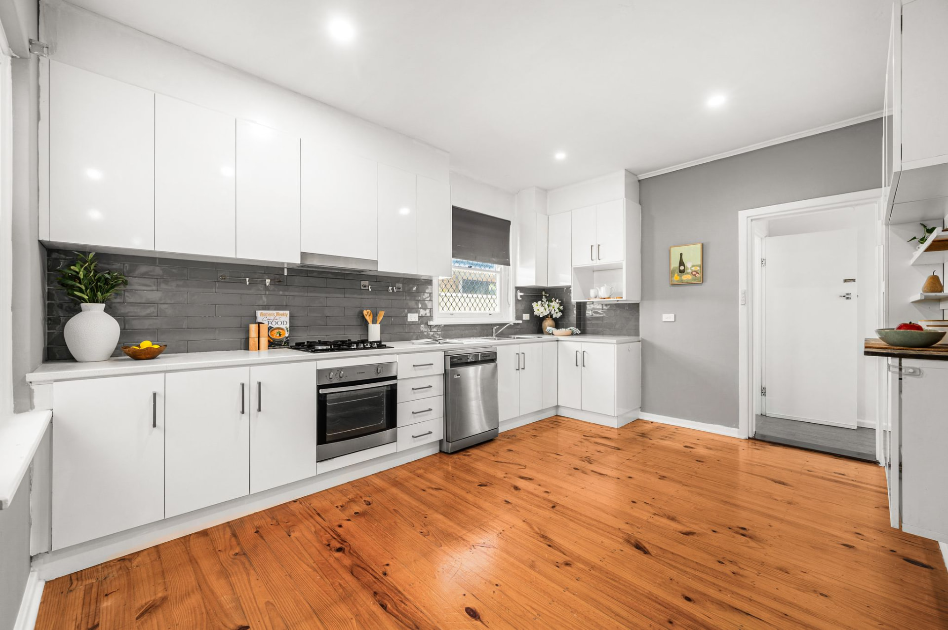 Modern kitchen with white cabinetry, dark grey subway-tile splashback, stainless steel appliances and polished timber floor
