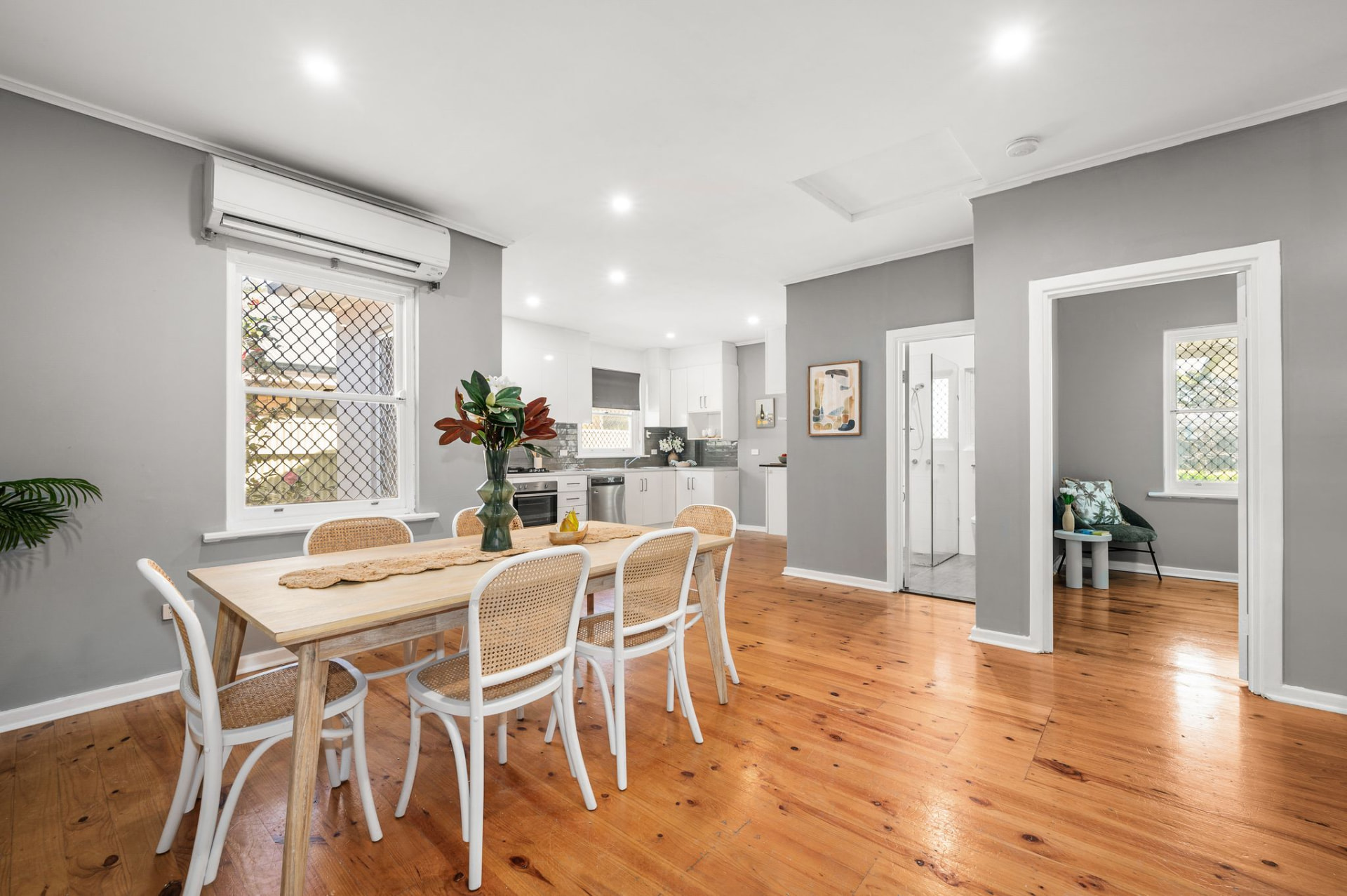 Open-plan dining area with a light-wood table and white wicker chairs, overlooking the kitchen and adjacent rooms
