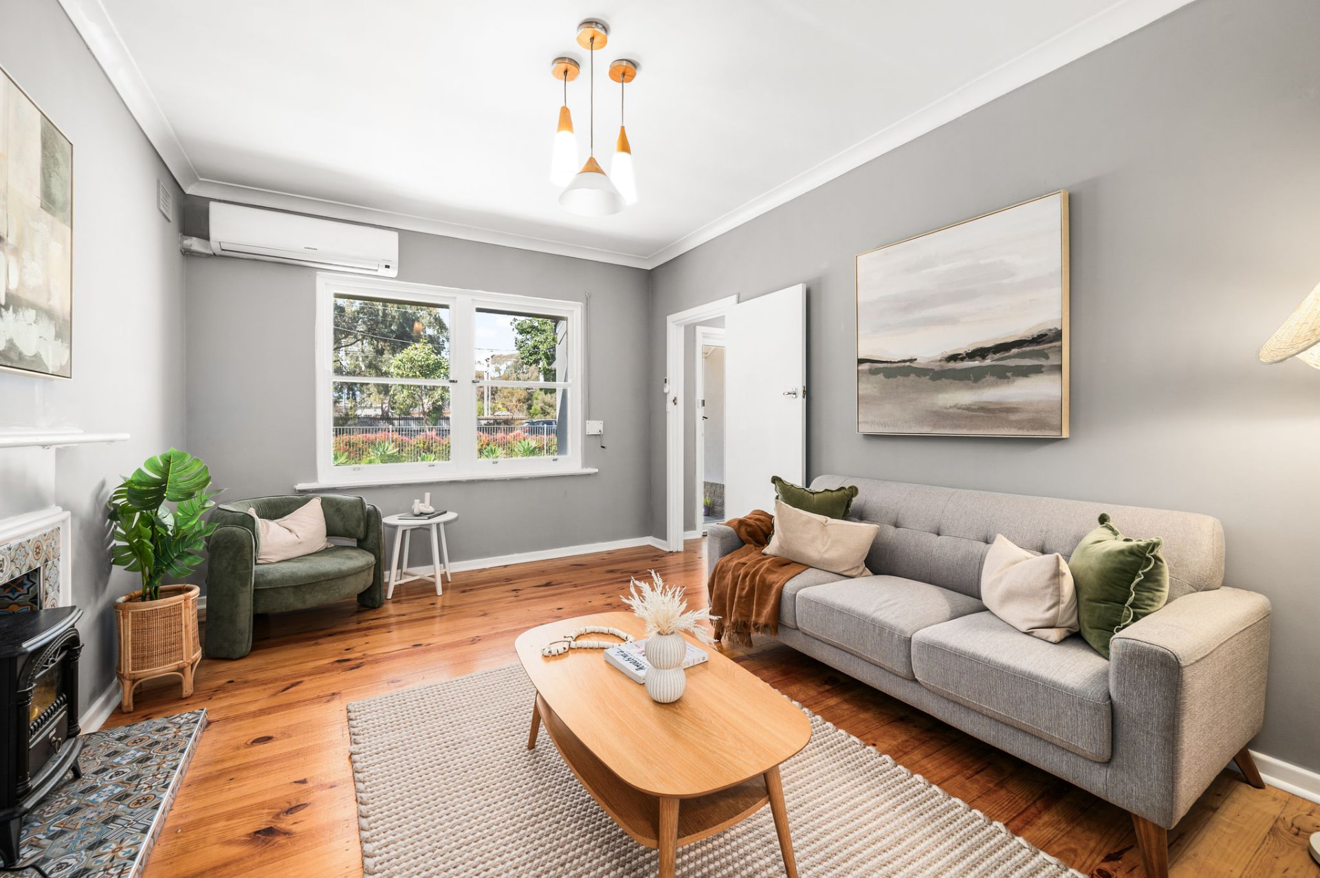 Living room with grey tufted sofa, green and cream cushions, light-wood coffee table and a fireplace with blue and white tile accents