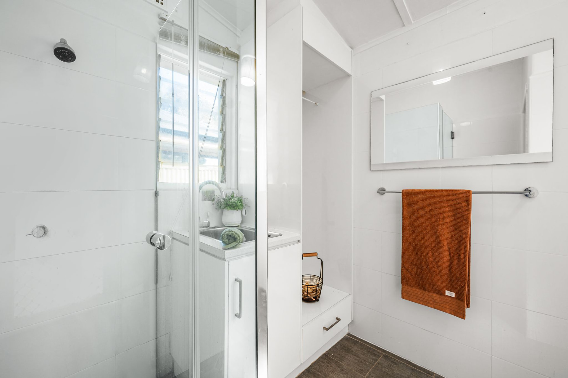 Bathroom and laundry area with glass-enclosed shower, white vanity, mirror and a chrome towel rack