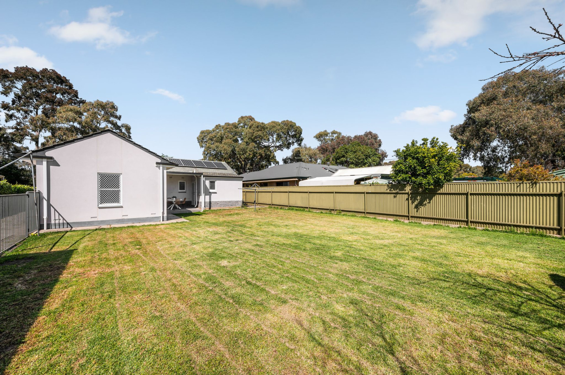 Backyard showing the expansive lawn bordered by a long corrugated metal fence, with the rear of the house visible
