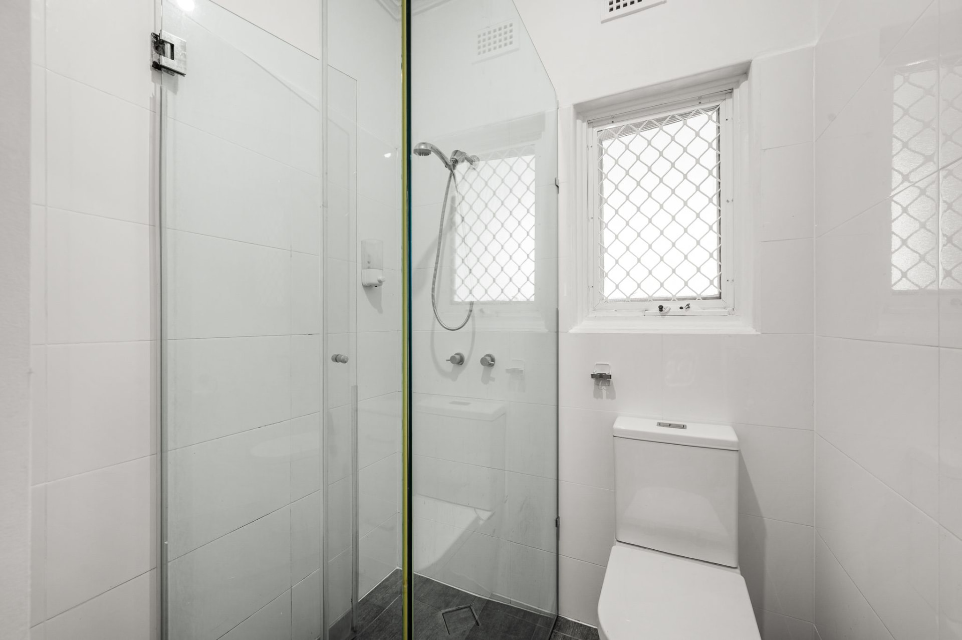 Bathroom with glass shower, white wall tiles, toilet and two windows